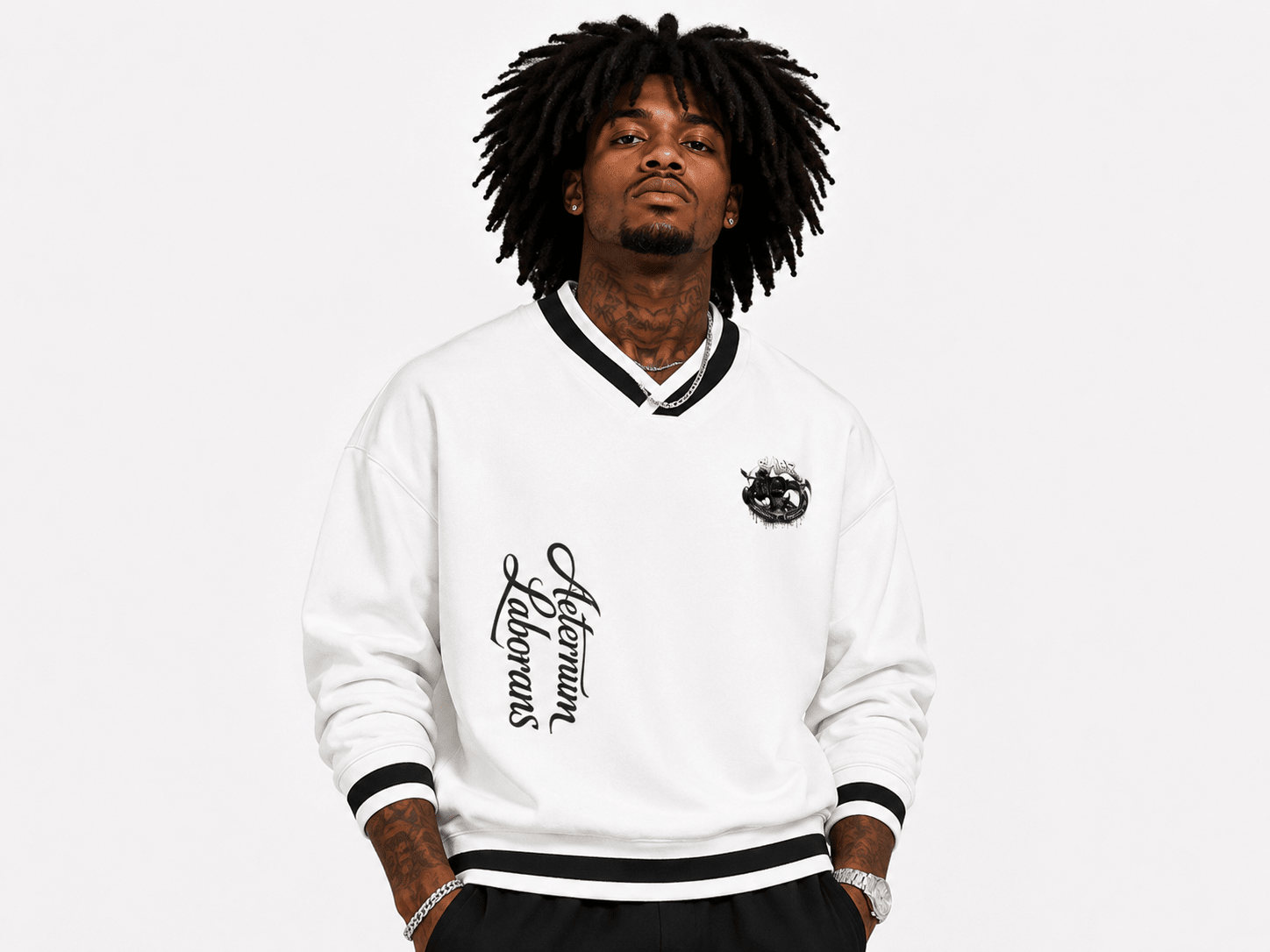 A man with dreadlocks wearing a white v-neck sweatshirt with black and white striped ribbed collar, cuffs, and hem, featuring a black script graphic on the right chest and a small circular graphic on the left chest. 