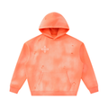 A distressed hoodie in a vibrant orange-coral color with a subtle tie-dye pattern, featuring a small white decorative emblem on the left chest. The hoodie has a front kangaroo pocket and is shown against a plain white background.