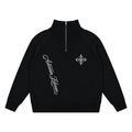 A black long-sleeve knit half-zip sweater with a mock neck, featuring white embroidered script on the right chest and a white fleur-de-lis motif on the left chest, displayed on a solid white background.
