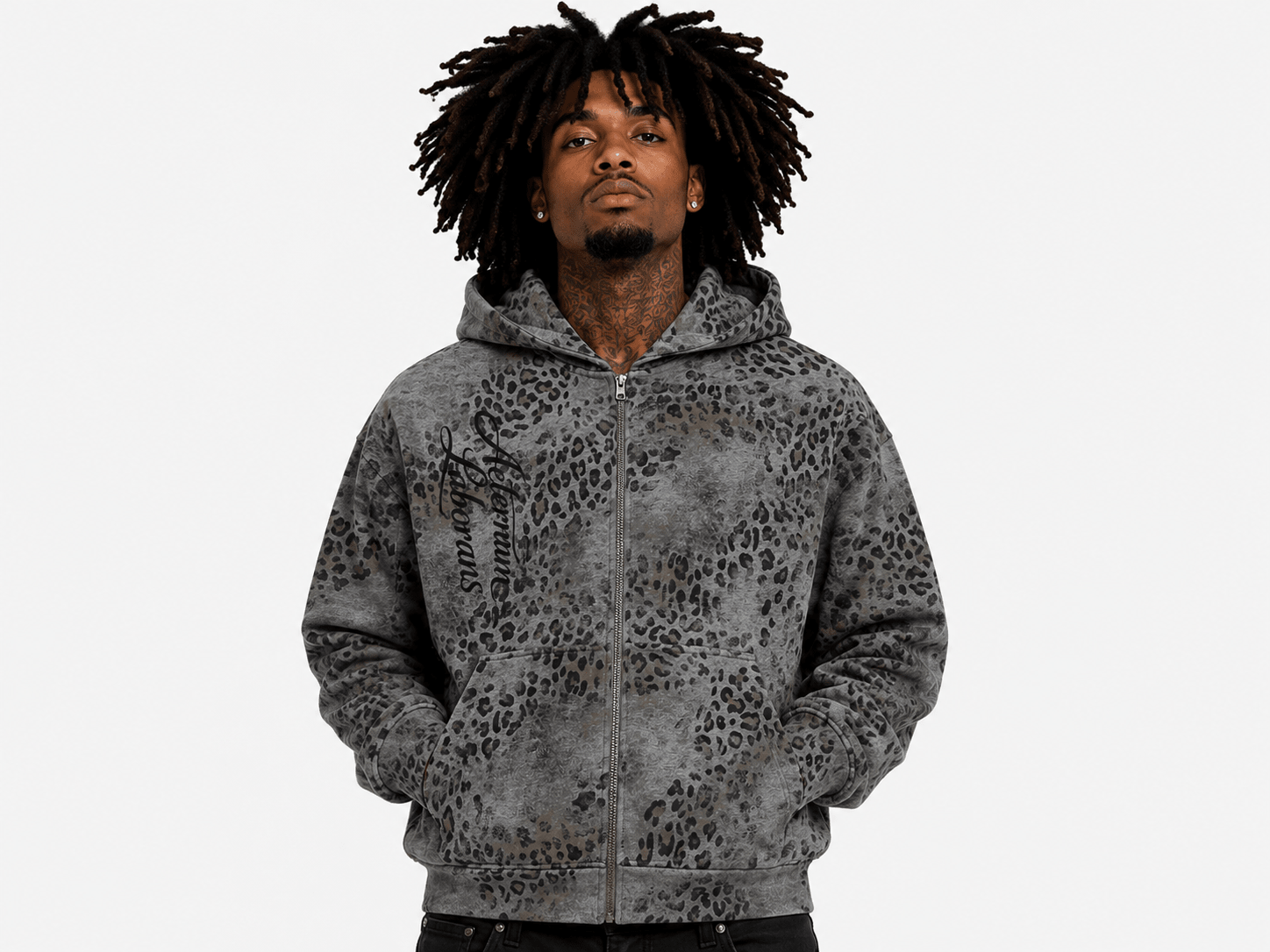 A man with dark dreadlocks wearing a gray and black leopard-print zip-up hoodie, photographed against a solid light gray background.