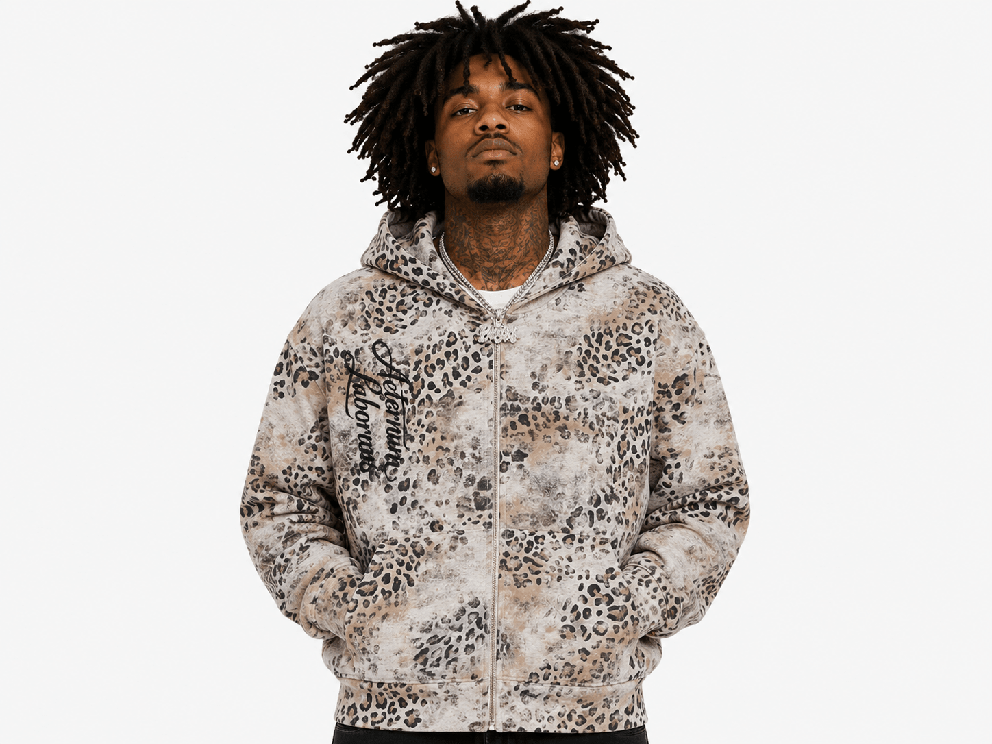A man with dreadlocks wearing a zip-up hoodie with a beige, brown, and black leopard print pattern, standing against a light gray background.
