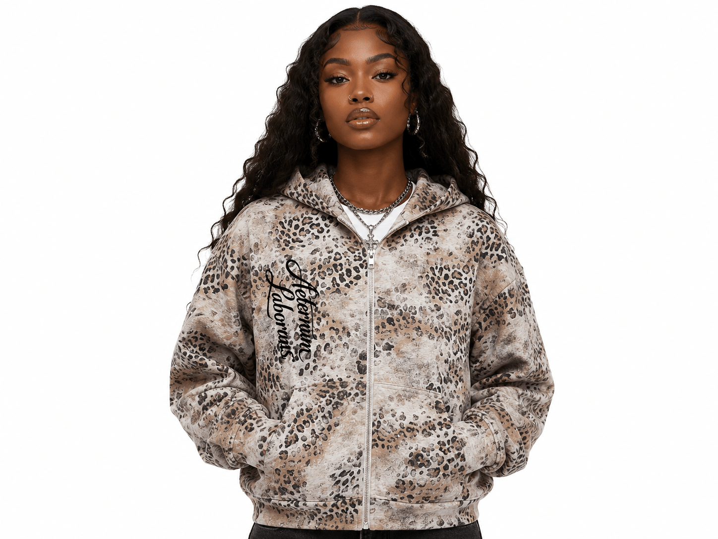 A woman modeling a zip-up hoodie with an animal print pattern in beige, brown, and black, featuring a black script graphic on the left chest, set against a plain white background.