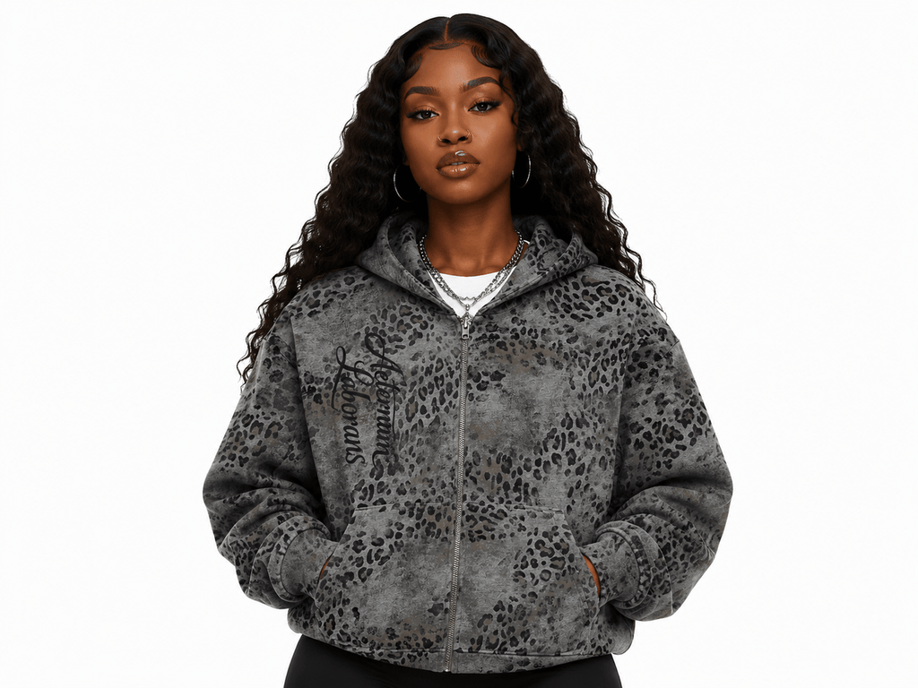 A woman modeling a gray leopard-print zip-up hoodie with black script text on the left chest, photographed against a plain white background.
