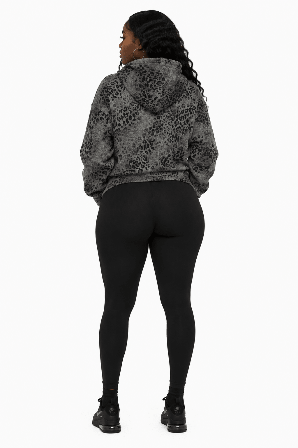 A woman shown from the back wearing a black and gray leopard-print hooded sweatshirt and black leggings, standing against a plain white background.