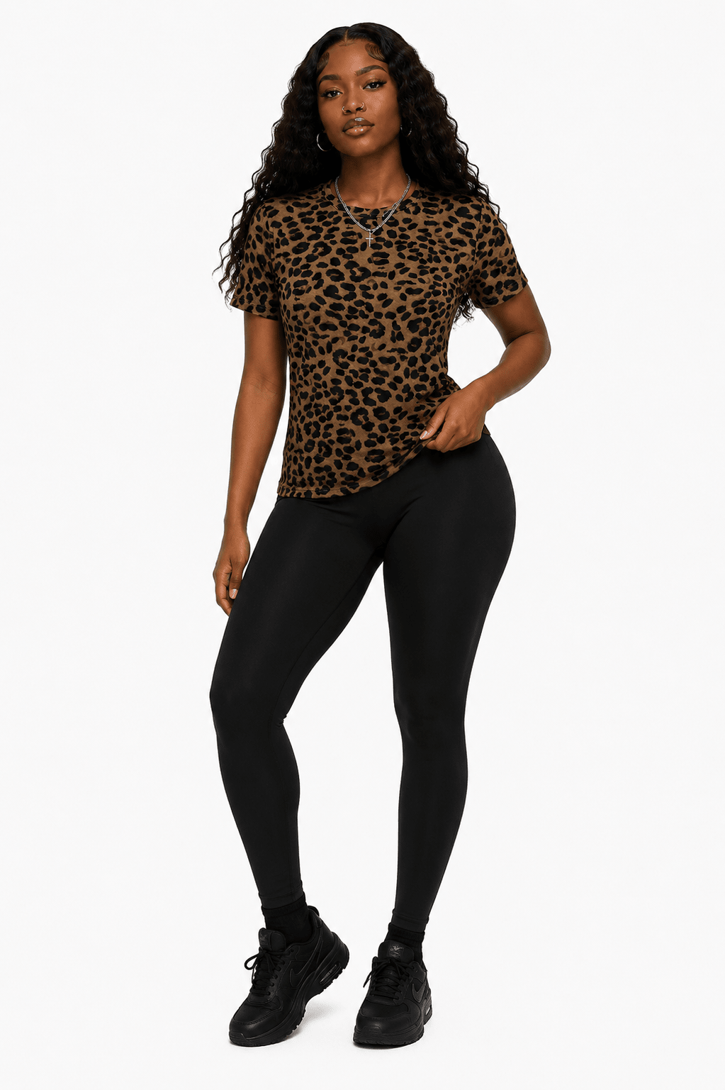 A woman modeling a short-sleeve crewneck t-shirt with a brown and black leopard print, paired with black leggings and black sneakers, against a plain white background.