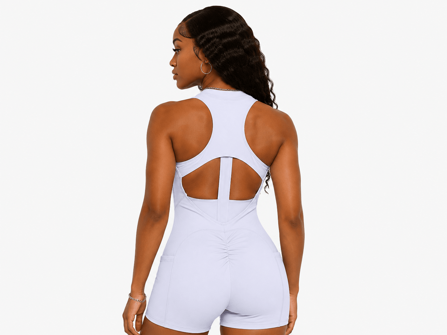 A woman shown from the back wearing a white one-piece athletic romper with a crossover back design and cutout details, against a plain light gray background.