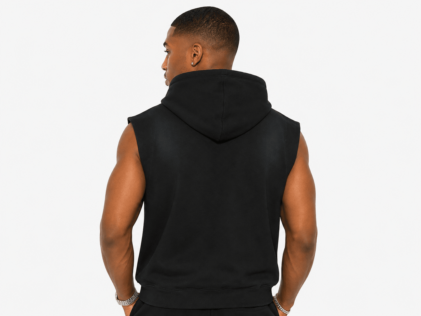 A man viewed from the back wearing a black sleeveless hooded top, photographed against a plain light gray studio background.
