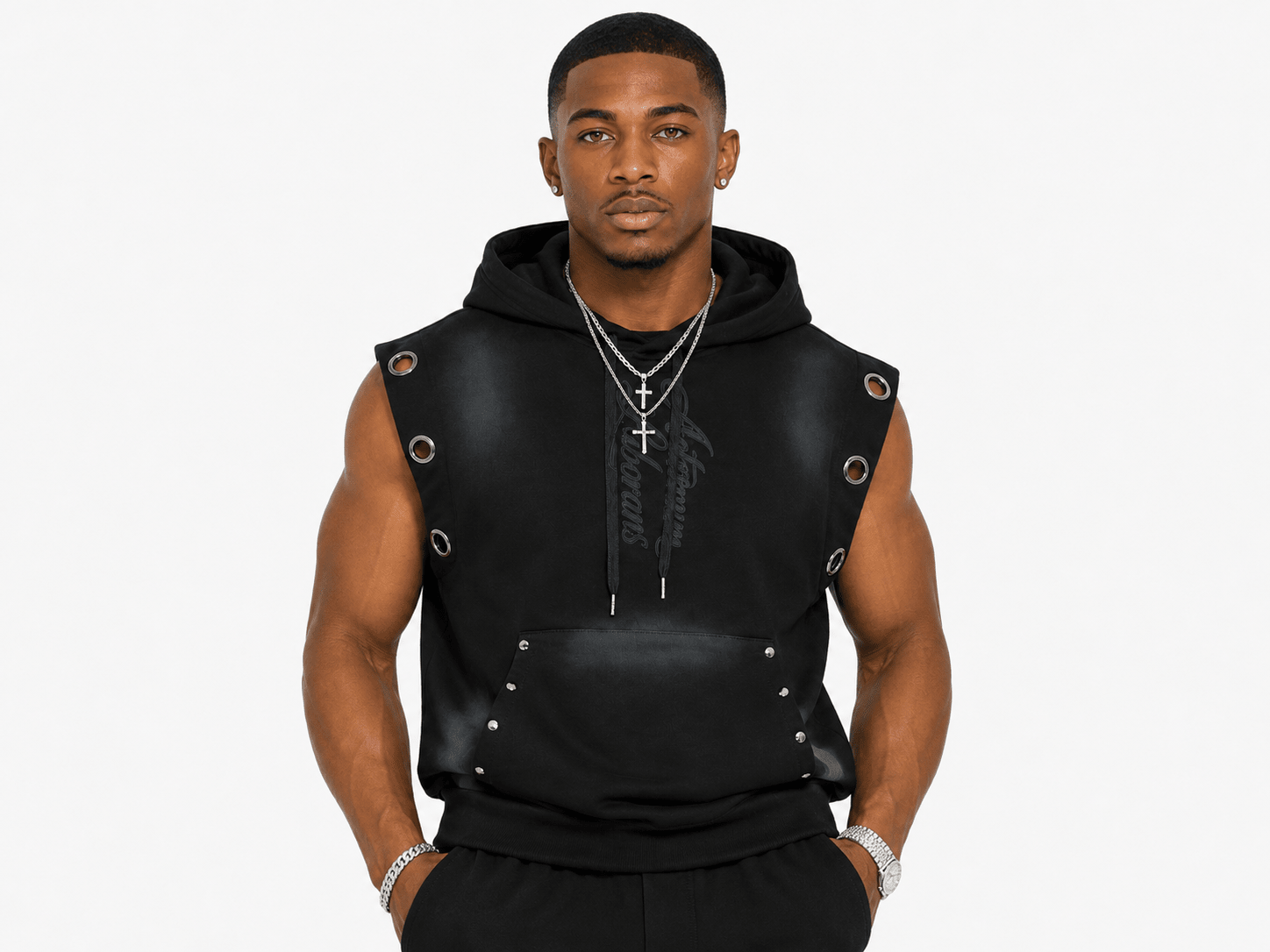 A man modeling a black sleeveless hooded sweatshirt vest with faux-leather panels, metal grommets, and silver chain necklaces against a plain white background.