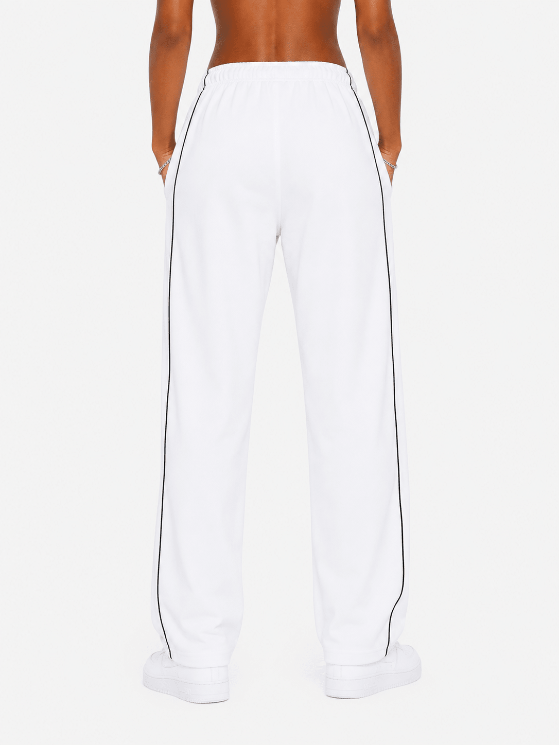 White wide-leg sweatpants with black side piping, shown from the back on a model against a light gray studio background.