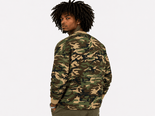 A man with dark curly hair is shown from the back wearing a long-sleeve crewneck sweatshirt with a classic green, brown, and tan camouflage pattern, set against a plain light gray background.