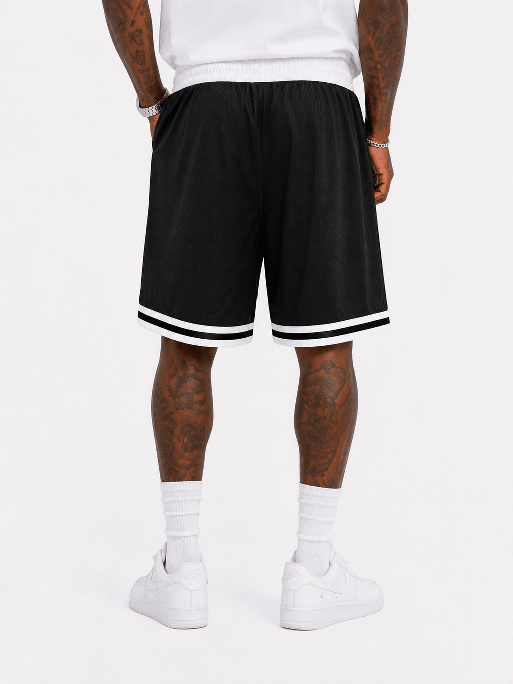 Black athletic shorts with white stripes on the hem, worn by a model with white sneakers and white crew socks against a light gray background.
