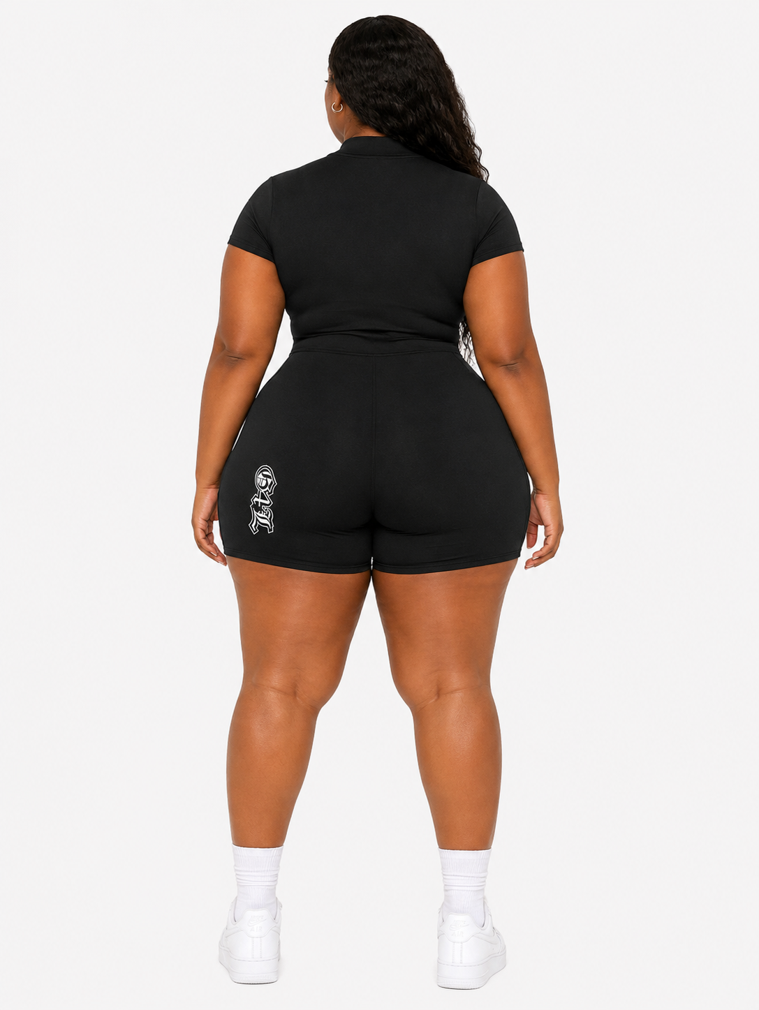 Person wearing a black outfit with a logo on shorts against a white background