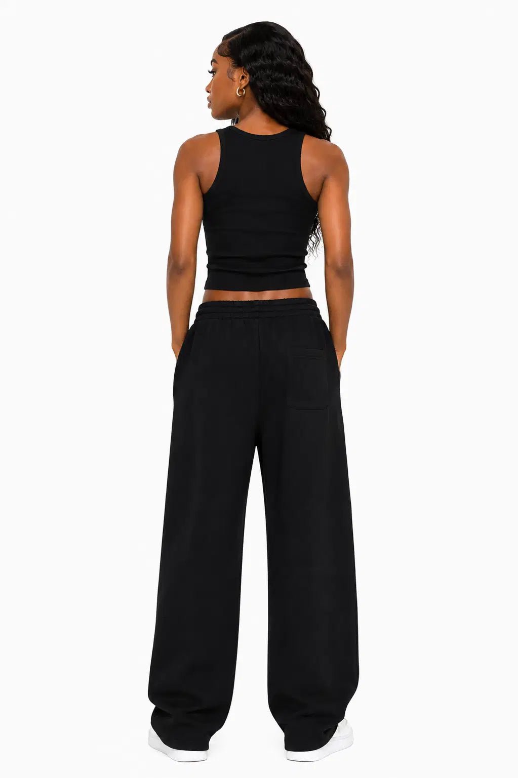 Person wearing a black tank top and wide-leg pants on a white background