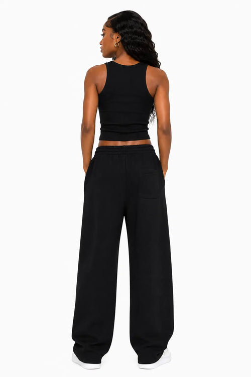 Person wearing a black tank top and wide-leg pants on a white background