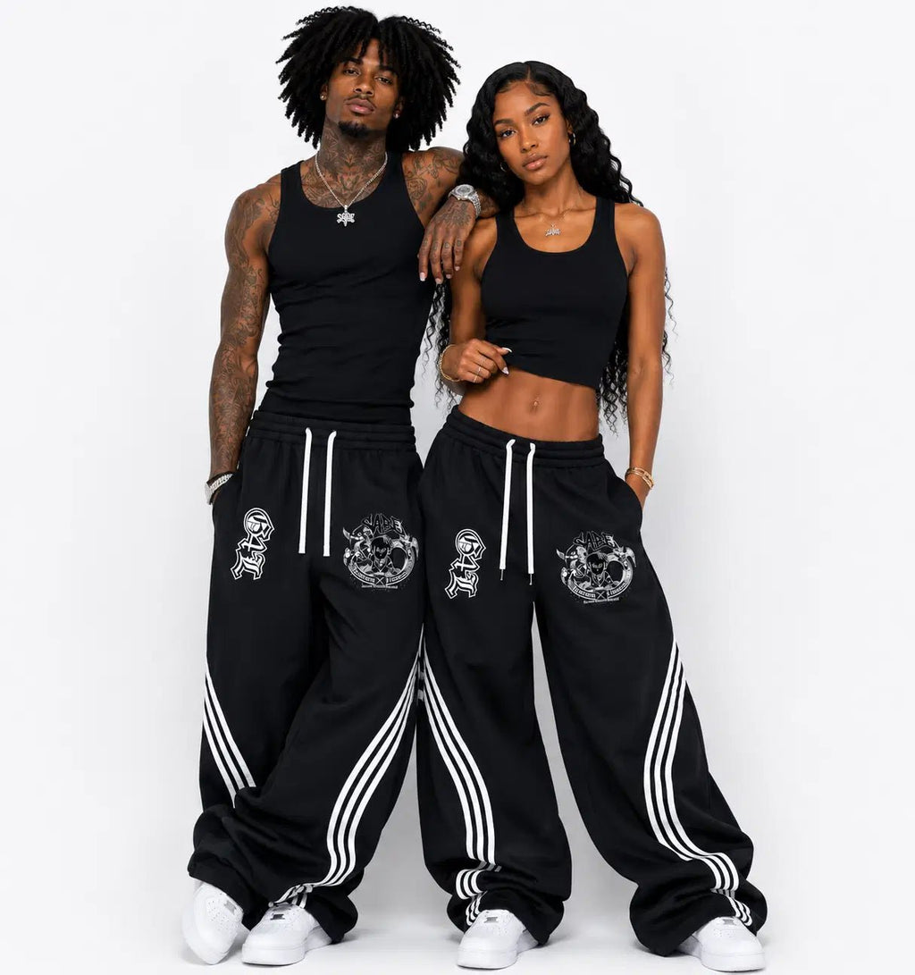 Two people wearing matching black tracksuits with white stripes on a white background