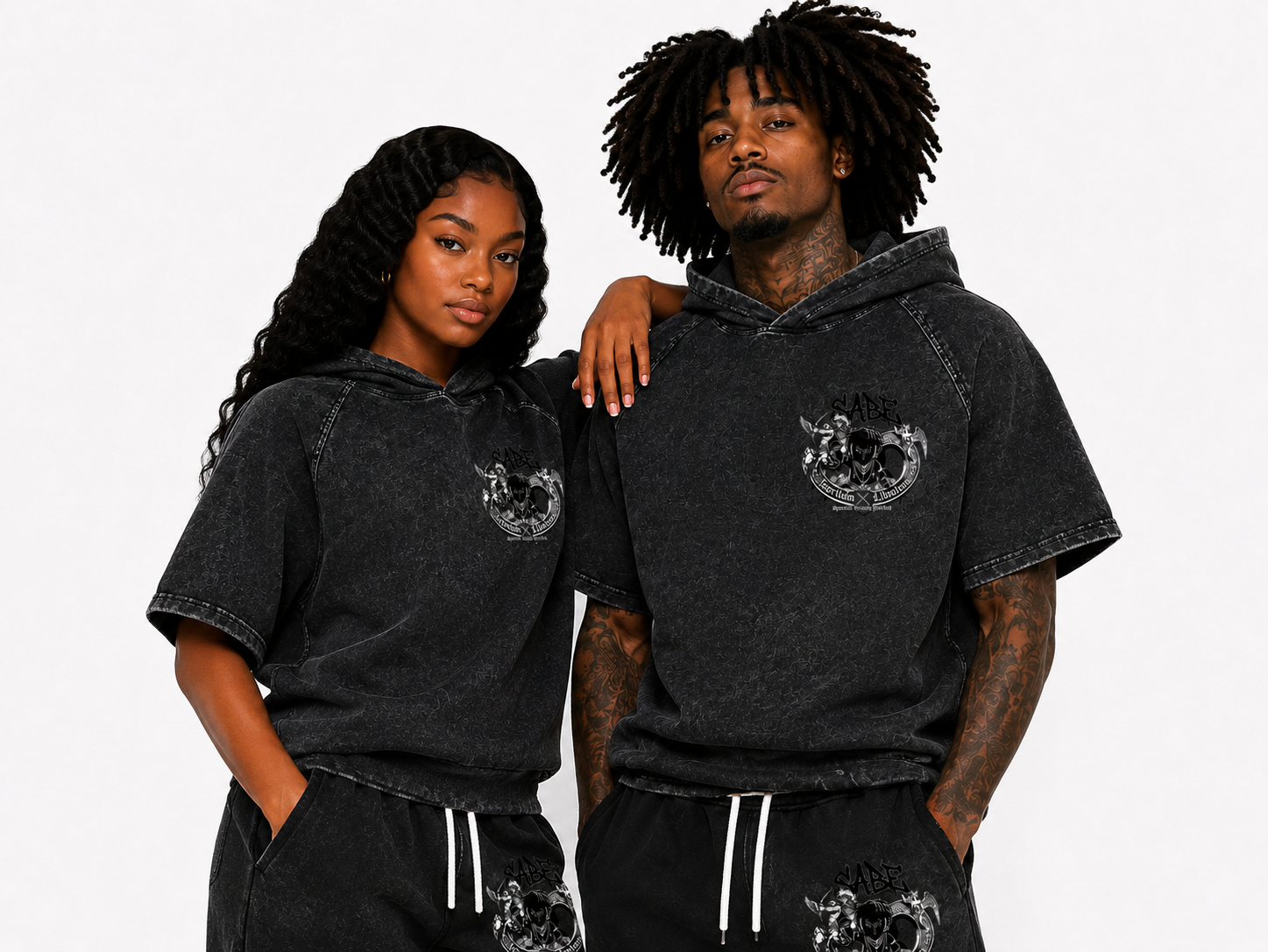 Two people wearing matching black hoodies with a logo on a white background