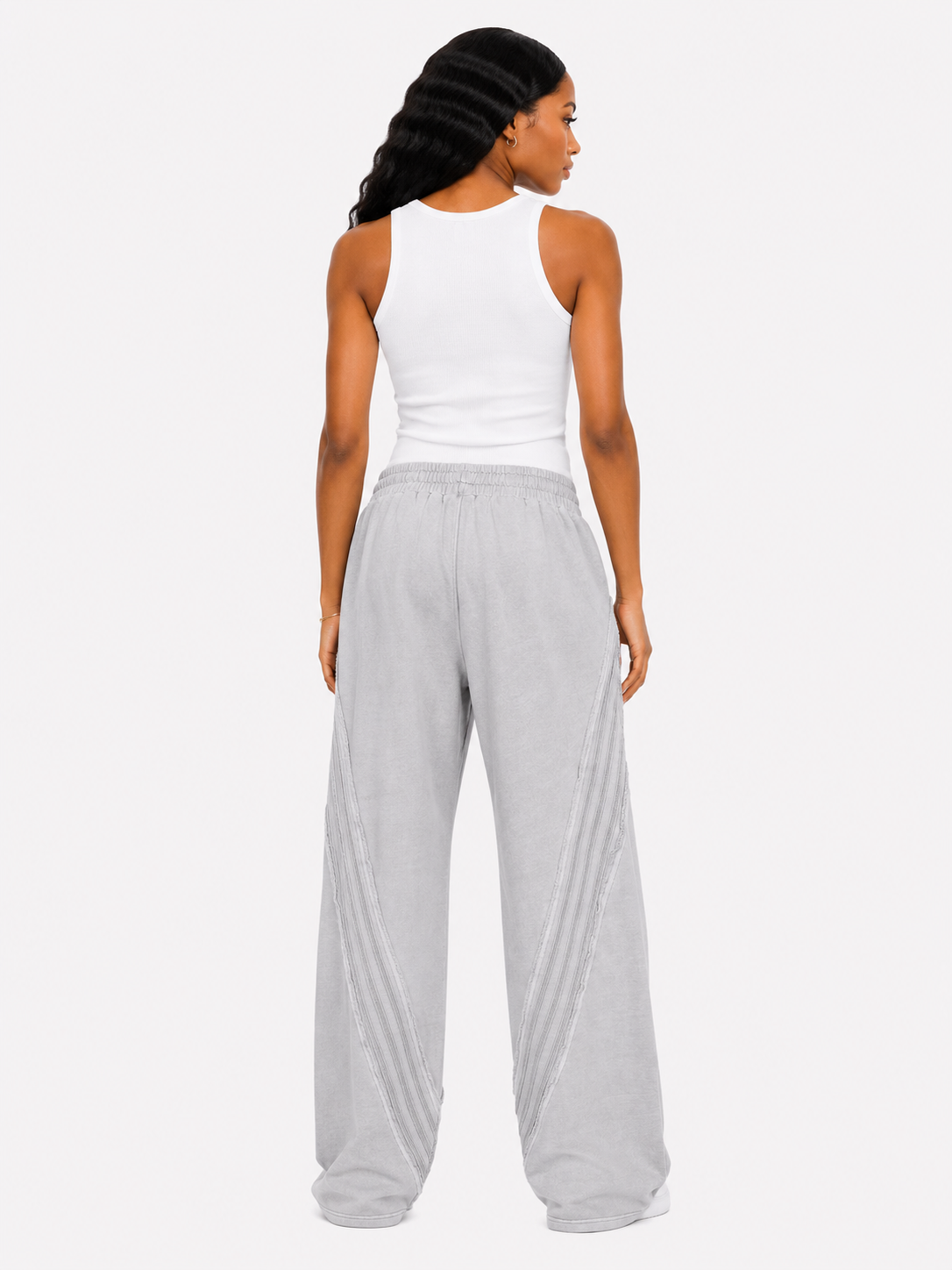 Woman wearing a white tank top and gray wide-leg pants on a white background