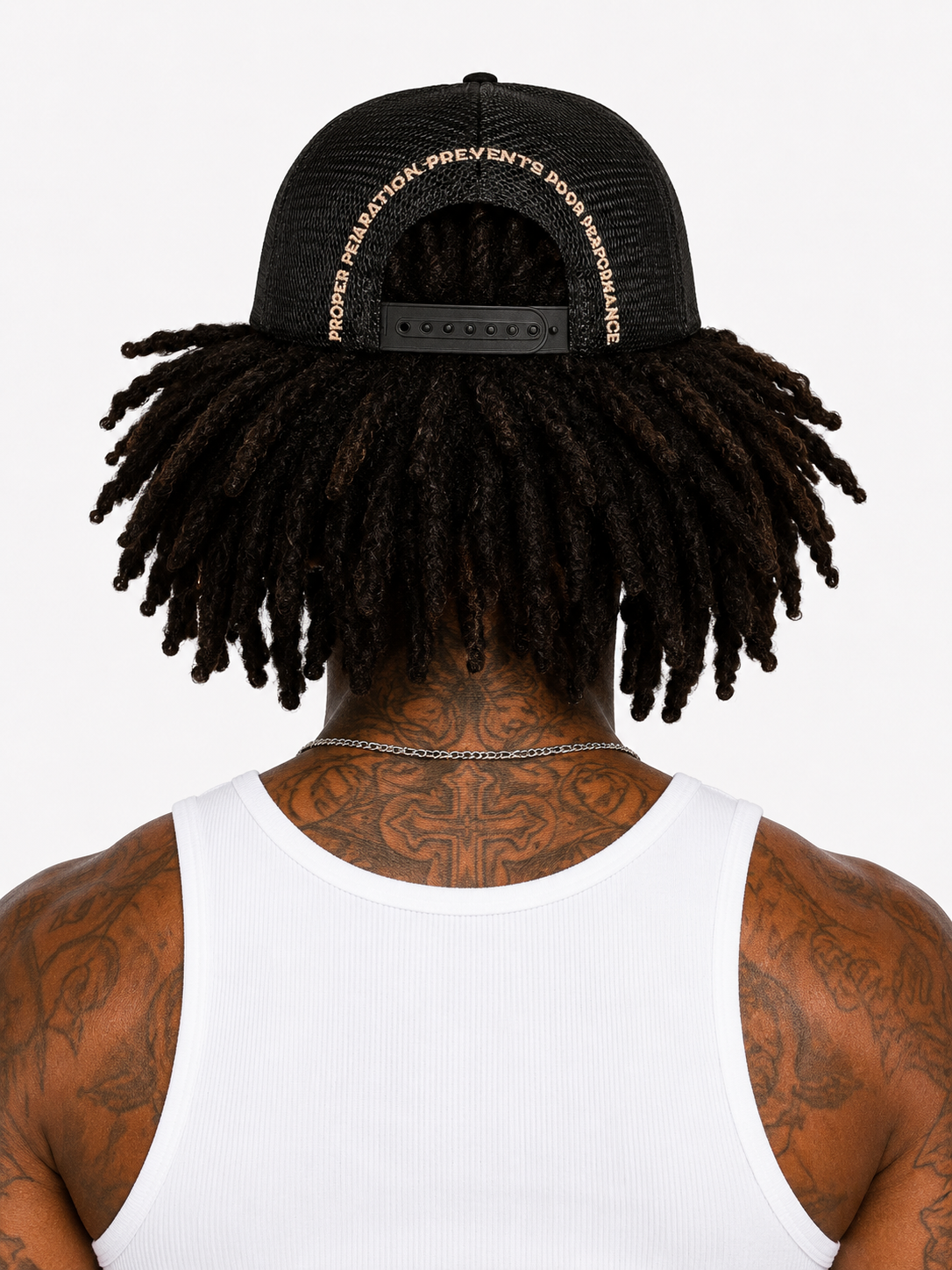 Person wearing a black cap with text, showing tattoos on the back of their neck and shoulders.