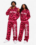 Two people wearing matching red camouflage tracksuits with text on a white background