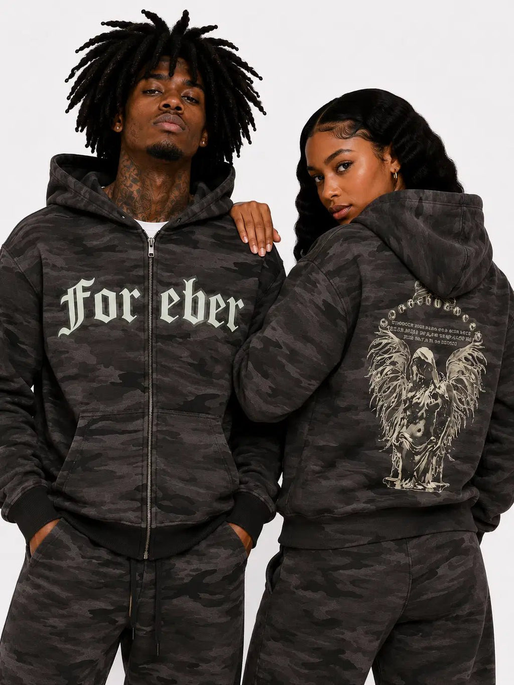 Two people wearing matching camouflage hoodies with text and graphics on a plain background