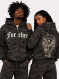 Two people wearing matching camouflage hoodies with text and graphics on a plain background