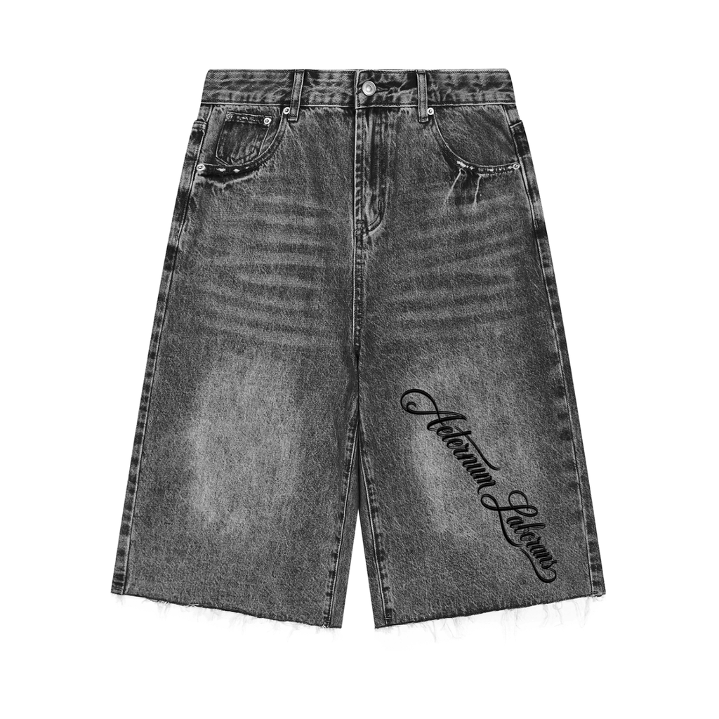 A pair of high-waisted, wide-leg denim shorts in a washed black/gray wash, featuring a black script embroidery reading 'Autumn Leaves' on the lower left leg. The shorts have a raw, frayed hem and are shown flat against a solid white background.
